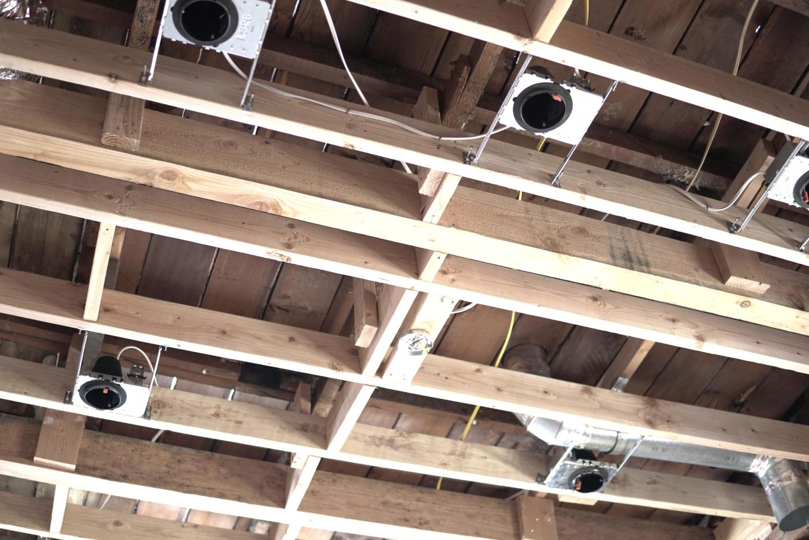 Exposed wooden ceiling frame with recessed lighting and electrical wiring during a home remodeling project.