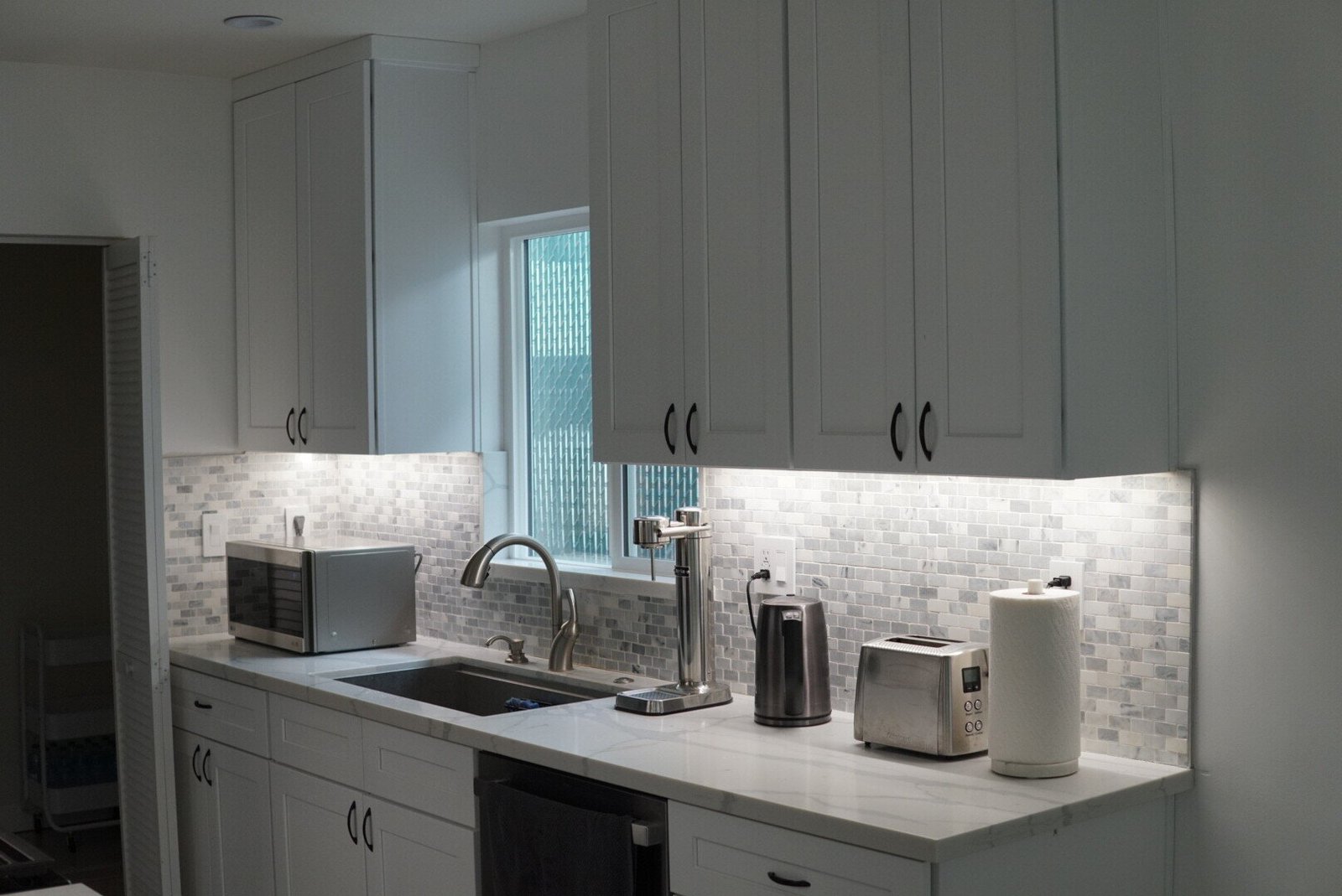 Warm under-cabinet lighting illuminating a modern kitchen remodel with a soft glow at night.