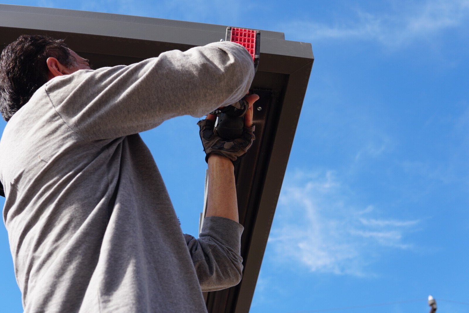 LAProElectrical technician installing outdoor lighting on a patio cover using a power drill under a clear blue sky.
