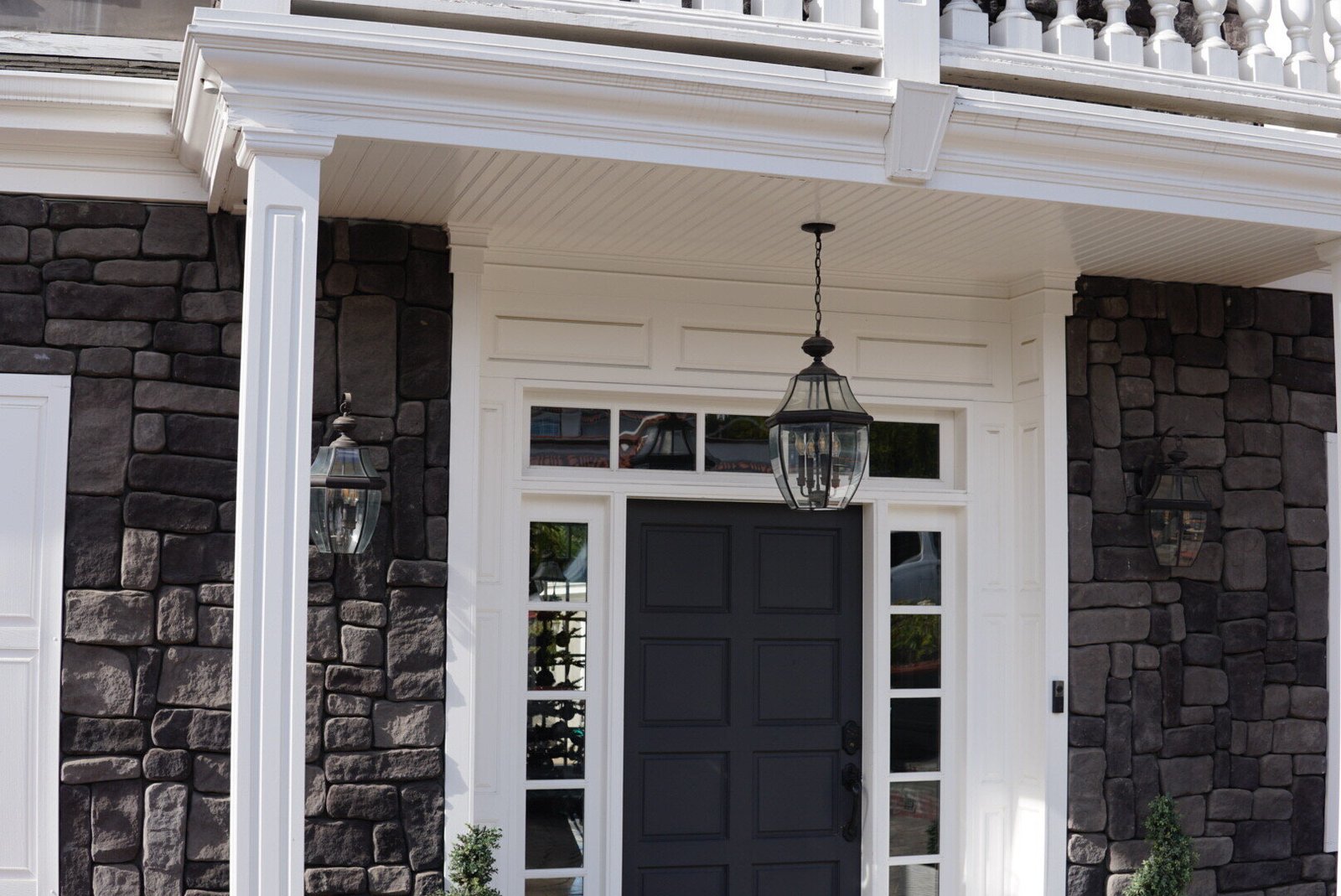Front entrance of a modern home with stone siding, a black door, and outdoor lantern-style lighting fixtures.