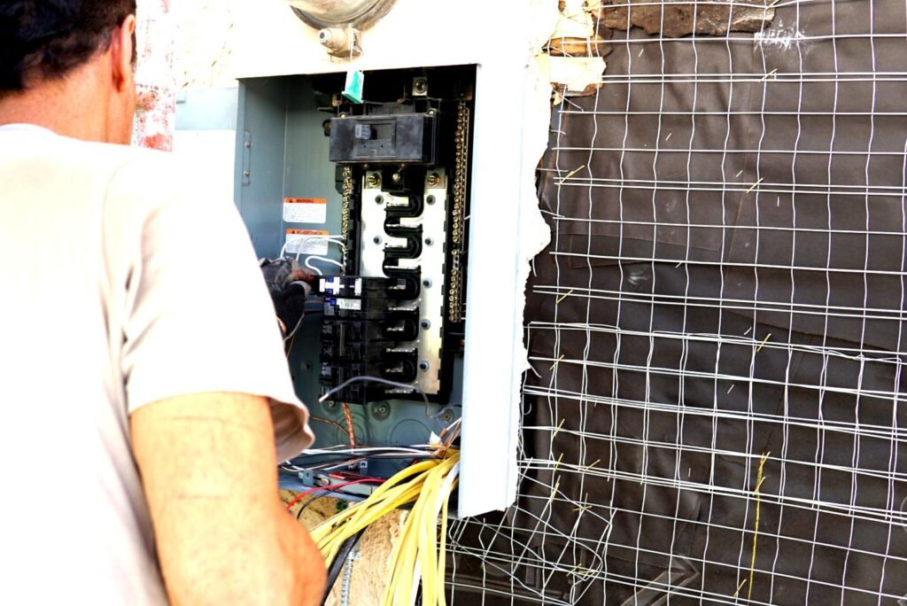 Electrician working on an open electrical panel with exposed wires during a residential construction project.