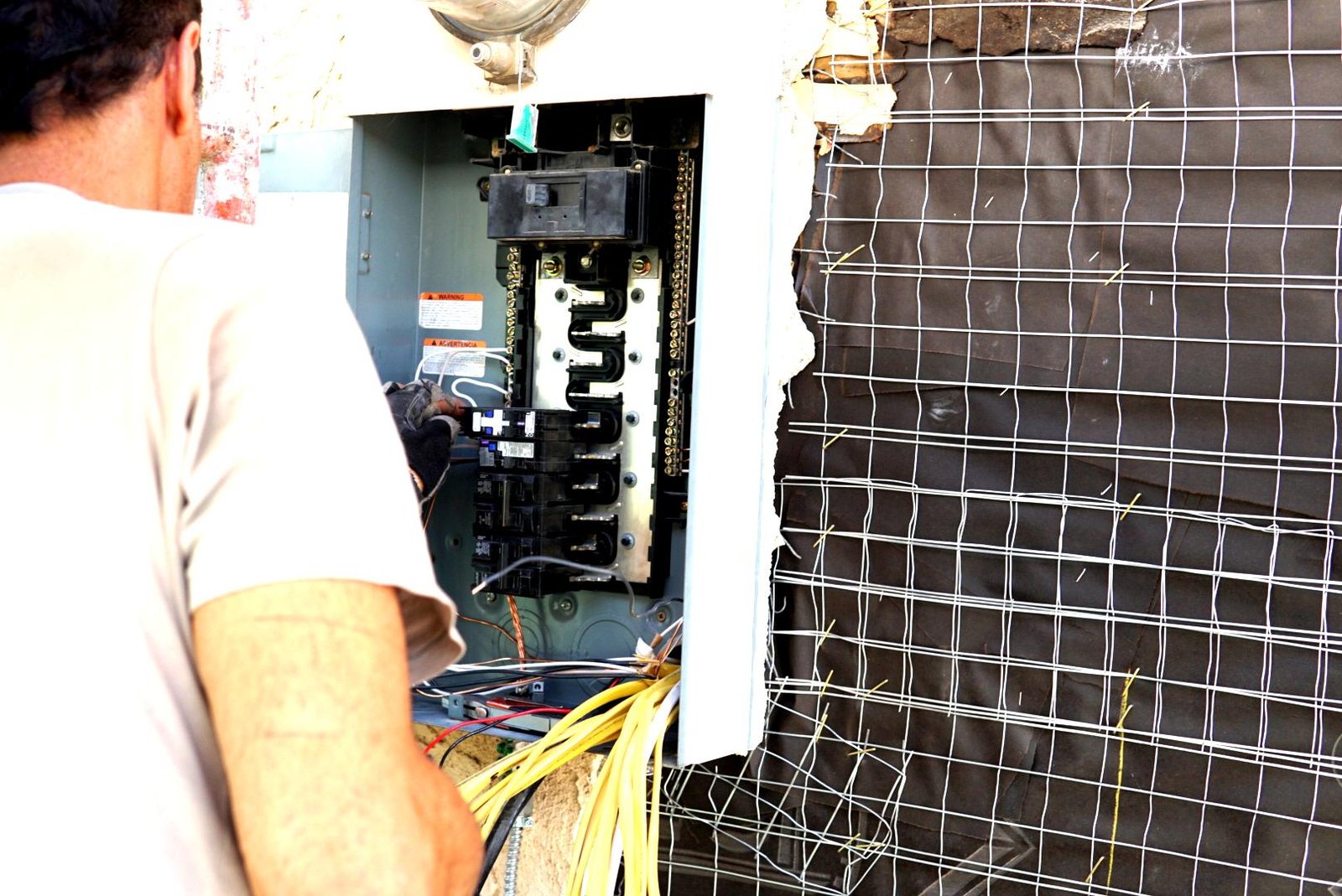 Electrician working on an open electrical panel with exposed wires during a residential construction project.